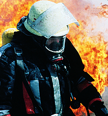 Ein Feuerwehrmann mit Atemmaske bewegt sich vor einem großen Feuer.